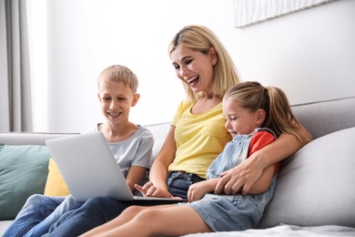 Happy mother using laptop with her children on sofa at home