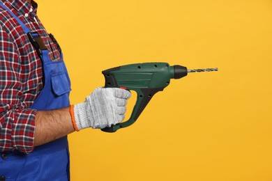 Worker in uniform with power drill on yellow background, closeup