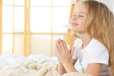 Photo of Girl with clasped hands praying on bed at home, space for text