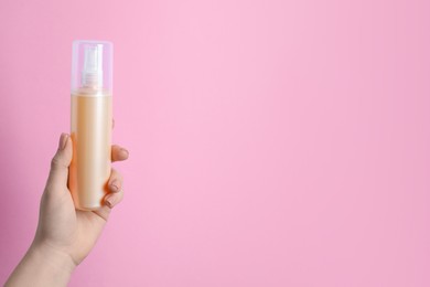 Photo of Woman holding spray bottle with thermal protection on light pink background, closeup. Space for text