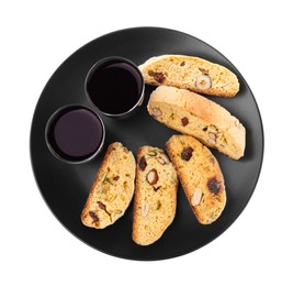 Black plate with tasty cantucci and glasses of liqueur on white background, top view. Traditional Italian almond biscuits