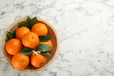 Delicious ripe oranges in bowl on white marble table, top view. Space for text