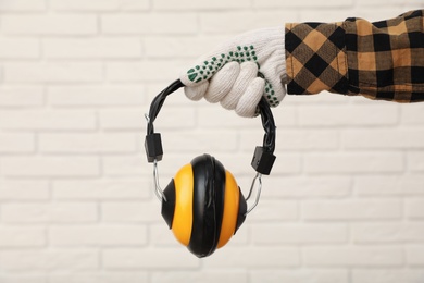 Worker holding safety headphones against white brick wall, closeup. Hearing protection device