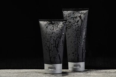 Wet tubes with men's cosmetic products on grey table against black background