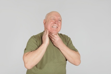 Senior man suffering from sore throat on light background. Enduring pain