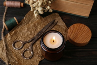 Photo of Burning scented candle, old scissors, book, threads and flowers on wooden table