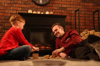 Photo of Happy father and son playing together on floor near fireplace at home