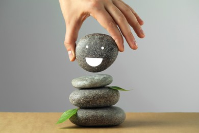 Woman putting stone drawn happy face onto stack against grey background, closeup. Zen concept