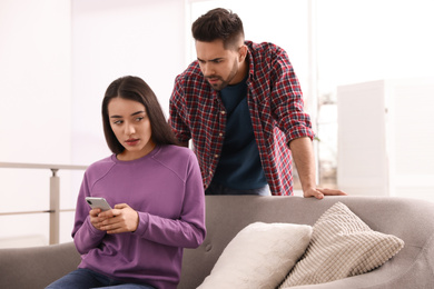 Distrustful young man peering into girlfriend's smartphone at home