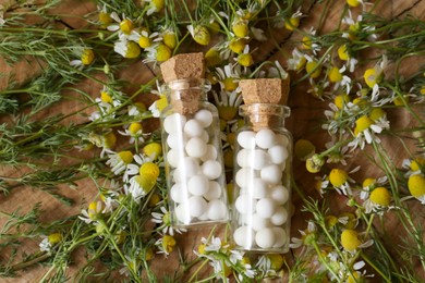 Bottles of homeopathic remedy and chamomile flowers on wooden background, flat lay