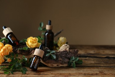 Photo of Bottles of rose essential oil and flowers on wooden table. Space for text