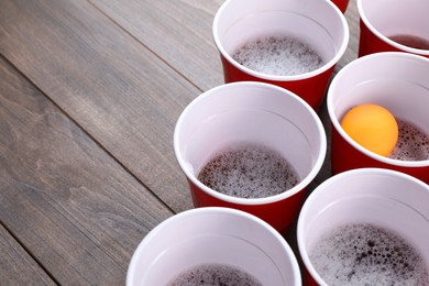 Photo of Plastic cups and ball on wooden table, space for text. Beer pong game
