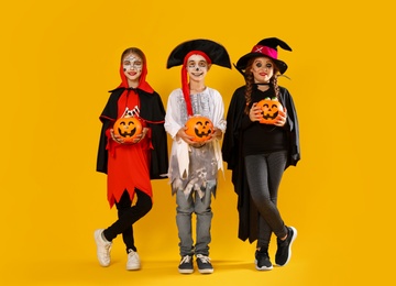 Cute little kids with pumpkin candy buckets wearing Halloween costumes on yellow background