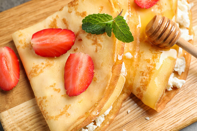 Photo of Delicious thin pancakes with strawberries, cottage cheese and honey on wooden board, closeup