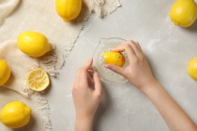 Young woman squeezing lemon with juicer on light table
