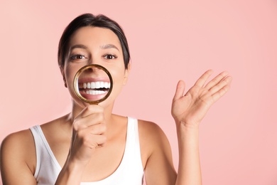 Young woman with healthy teeth and magnifier on color background