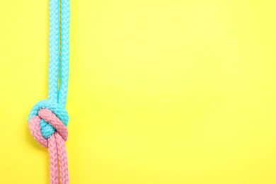 Top view of colorful ropes tied together on yellow background, space for text. Unity concept