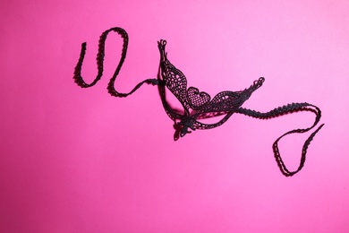Black lace mask on pink background, top view with space for text. Sexual role play accessory