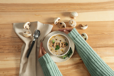 Woman with fresh mushroom soup at wooden table, top view