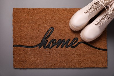 Photo of Doormat with word Home and stylish boots on grey background, flat lay