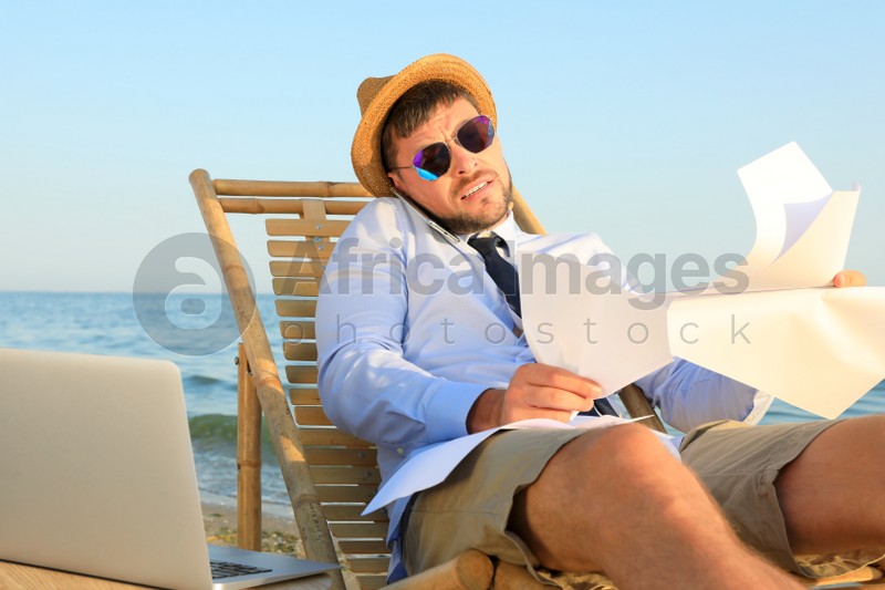 Busy man with papers talking by mobile phone on beach. Business trip