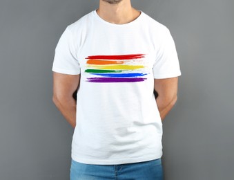 Young man wearing white t-shirt with image of LGBT pride flag on grey background