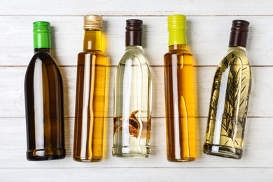 Different sorts of cooking oil in bottles on white wooden table, flat lay