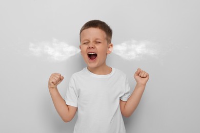 Aggressive little boy with steam coming out of his ears on grey background