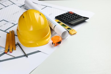 Construction drawings, safety hat, calculator, tape measure, folding ruler and bubble level on white background. Space for text
