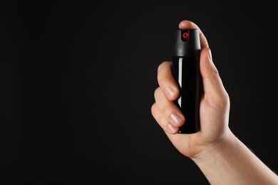 Man holding pepper spray on black background, closeup. Space for text