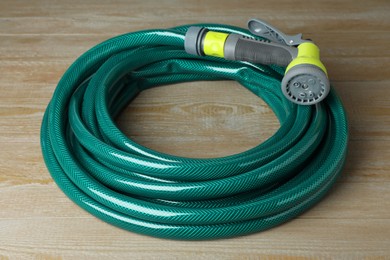 Green rubber watering hose with nozzle on wooden surface