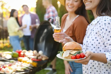Photo of Group of friends having barbecue party outdoors, space for text. Focus on burger
