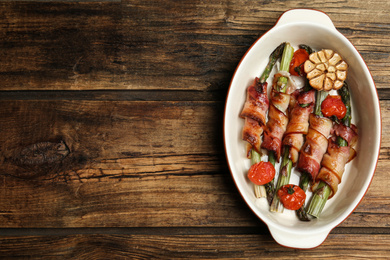 Oven baked asparagus wrapped with bacon in ceramic dish on wooden table, top view. Space for text