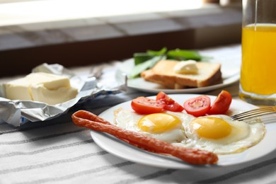 Tasty fried eggs with smoked sausages and tomatoes on table, closeup