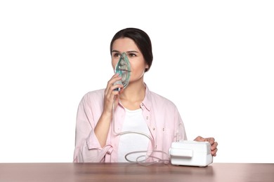 Young woman using nebulizer at wooden table on white background