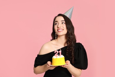 Photo of Coming of age party - 21st birthday. Smiling woman holding delicious cake with number shaped candles on pink background