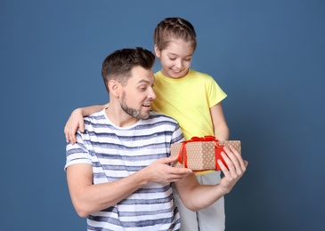 Man receiving gift for Father's Day from his daughter on color background