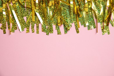 Golden tinsel on pink background, top view. Space for text