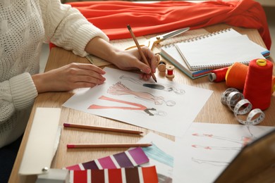 Fashion designer creating new clothes in sketchbook at wooden table, closeup