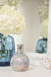 Stylish catalytic lamp with beautiful bouquet on white table near mirror. Cozy interior