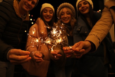 Group of people holding burning sparklers, focus on hands