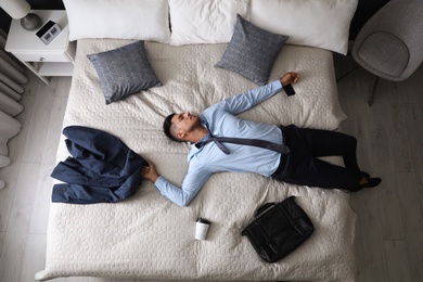 Exhausted businessman in office wear sleeping on bed at home after work, above view