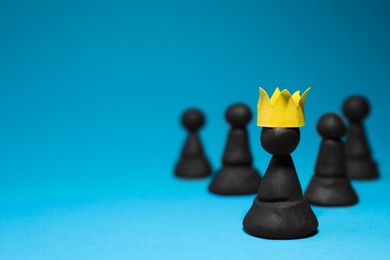 Black plasticine chess pieces and one with paper crown on light blue background, space for text