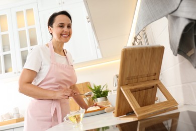 Woman making cake while watching online cooking course via tablet in kitchen