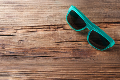 Stylish sunglasses on wooden background, top view. Space for text