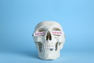 Photo of Information warfare concept, media propaganda influence. Paper cards with words news in eye sockets of human skull on light blue background
