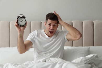 Emotional man with alarm clock in bed. Being late because of oversleeping