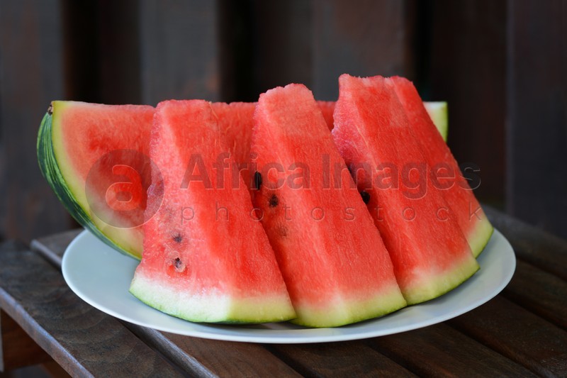 White plate with sliced watermelon on wooden stool outdoors