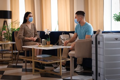Couple with medical face masks having conversation while waiting in hotel hall
