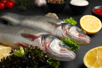 Photo of Fresh raw sea bass fish and ingredients on black table, closeup